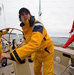 A maritime specialist in yellow storm gear controls a sailing yacht at sea